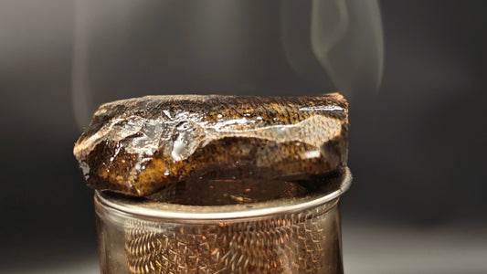 A macro close-up of premium sinking grade Kynam Agarwood naturally cultivated, showing rich dark lipids and waxy resin bubbling under heat with pristine translucent vapors