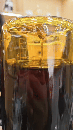 Viscous vintage Hainan Oud oil slowly dripping and hanging on the glass wall of an applicator, demonstrating high resin density and purity